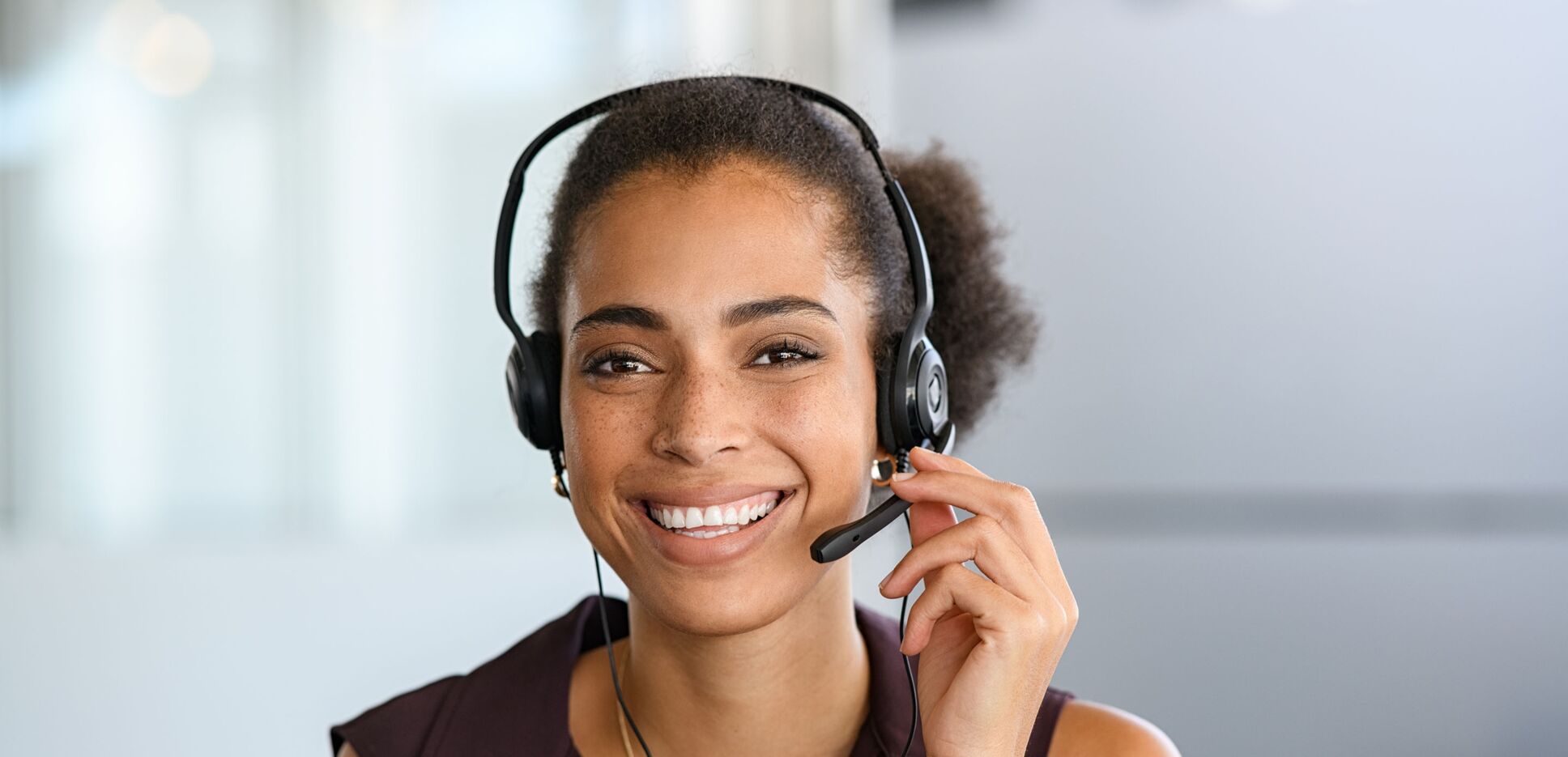 Mitarbeiterin im Gespräch mit Kunden über Headset mit Blick auf die Kamera.